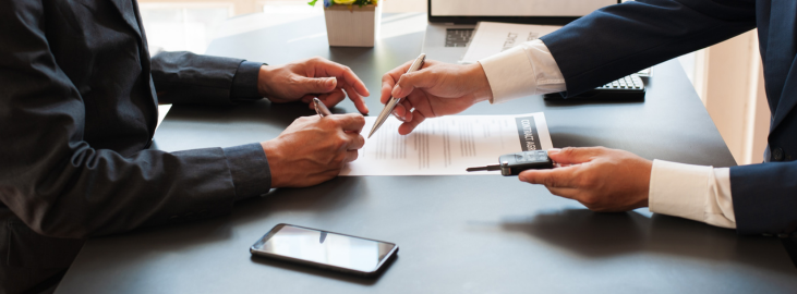 Picture of two men signing lease with key and lease agreement on a desk in a modern office with natural lighting
